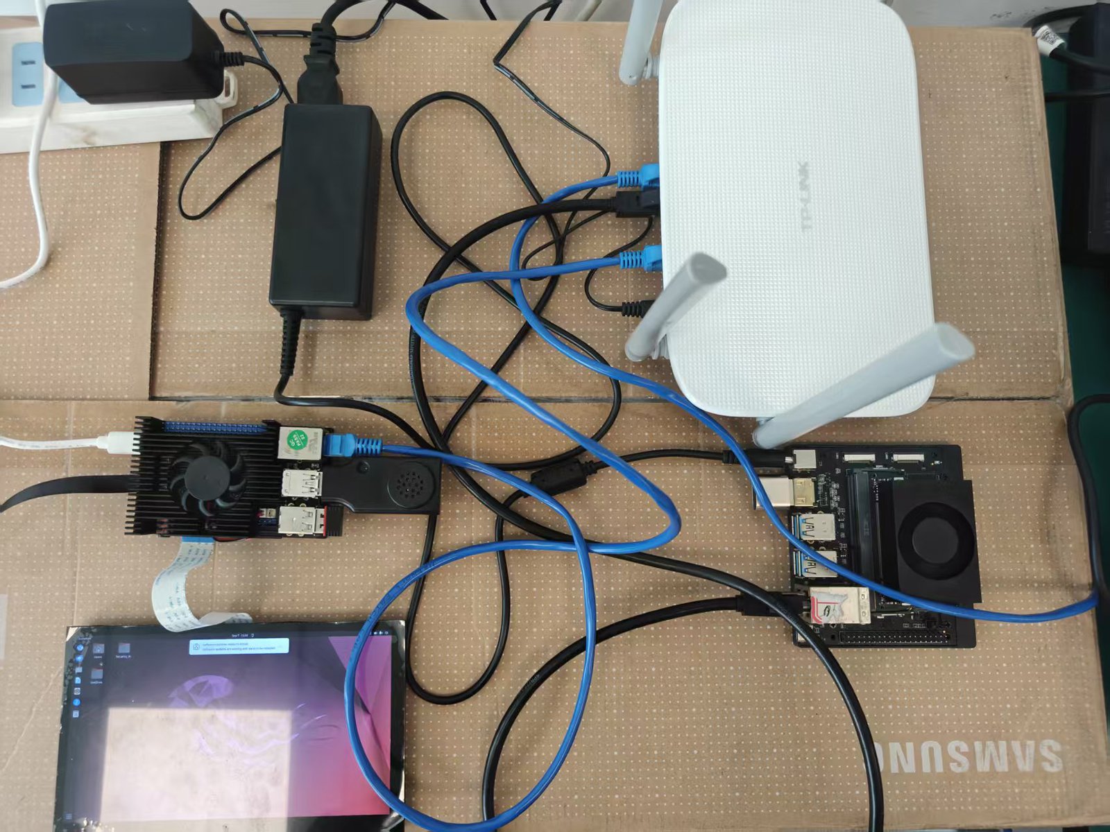 双板实物:左上 Jetson Orin Nano、右侧 RK3588 LubanCat-4、左下 7 寸 DSI 触摸屏(座舱 UI 运行中),两板经路由器以太网互联,麦克风/音箱 USB 组合设备接 RK